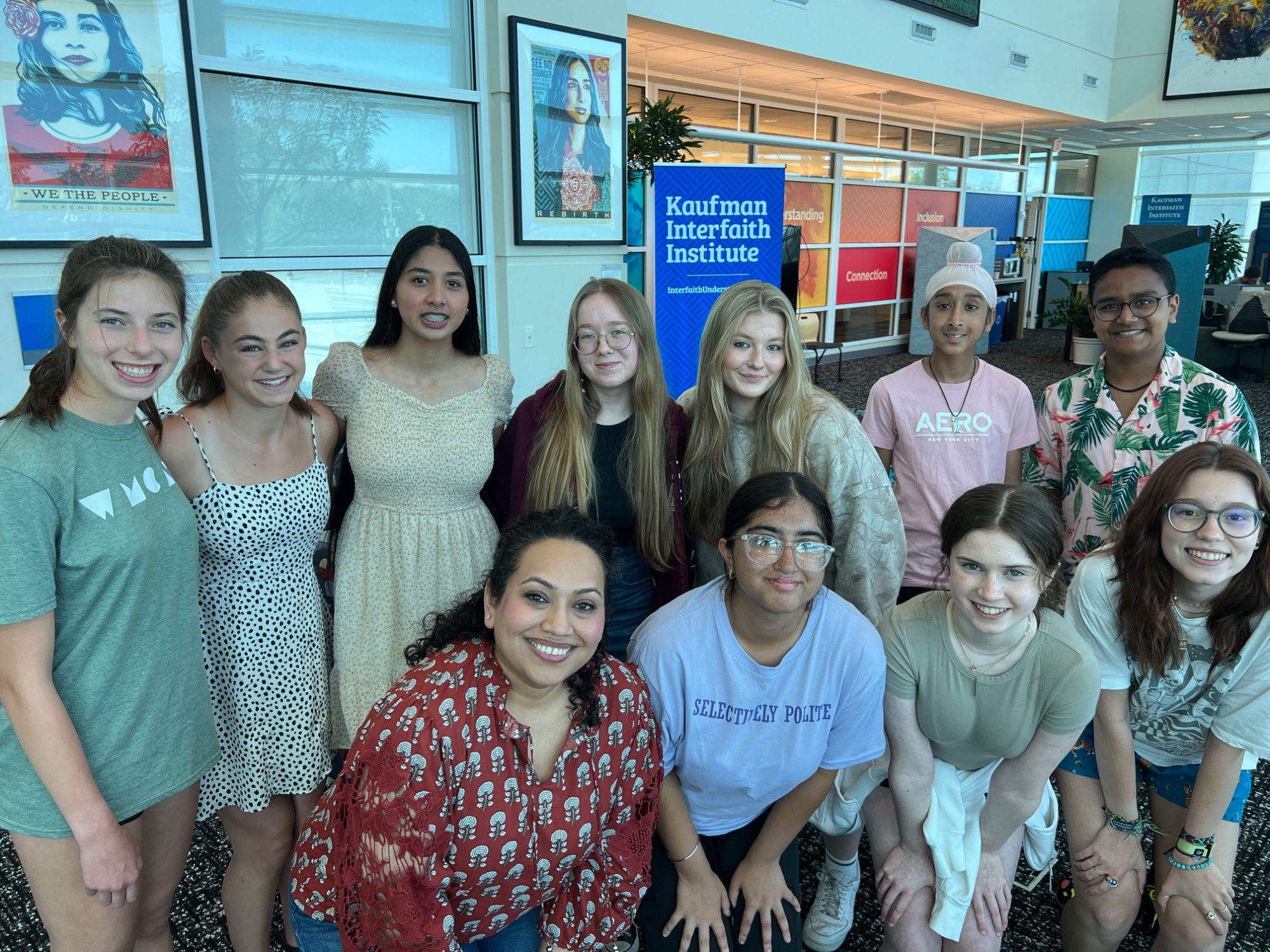 A group of teenagers in colorful clothing posing for a photo with their Kaufman staff leader, Zahabia. This was our 2023-2024 cohort of Scholars.